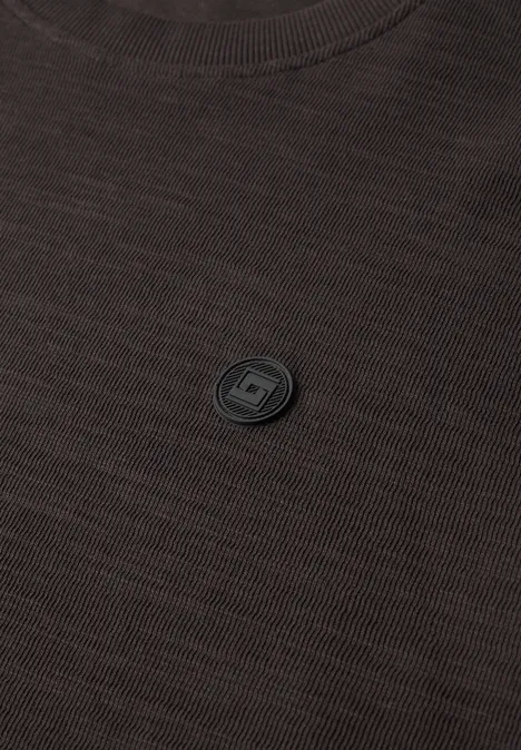 Dunkelbraunes T-Shirt mit kleinem schwarzem runden Emblem in der Mitte der Brust.