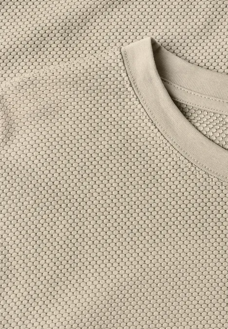 Gros plan sur un t-shirt beige à motif nid d’abeille.