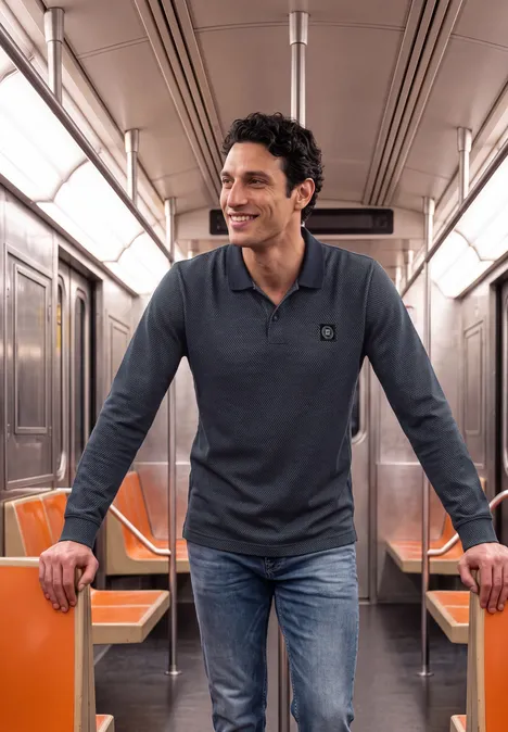 Un homme souriant en jean et polo se tient dans un métro aux sièges orange.