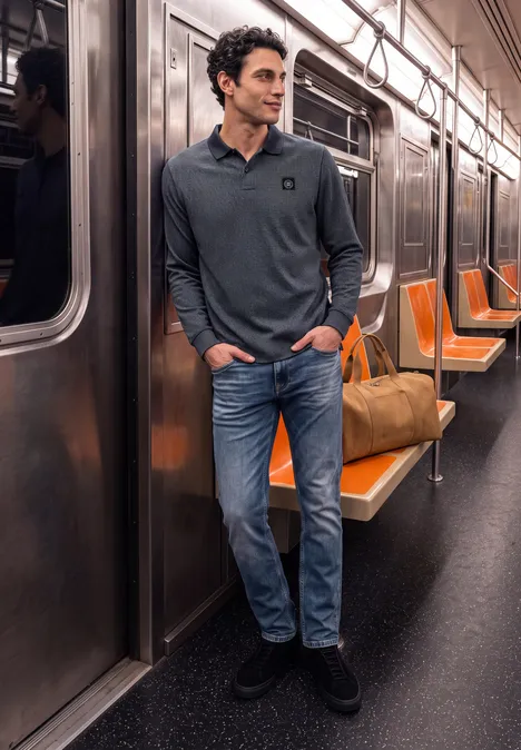 Un homme décontracté appuyé contre la porte d’un métro quasi vide aux sièges orange, son sac de voyage à ses côtés.