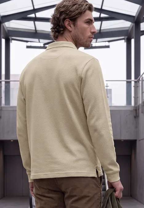 Un homme en veste beige de dos dans un couloir moderne avec verrière, regard par-dessus l’épaule.