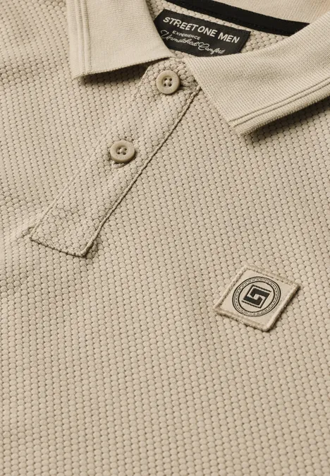 Polo beige texturé avec col rayé, patte de boutonnage et petite plaque d’emblème de marque.