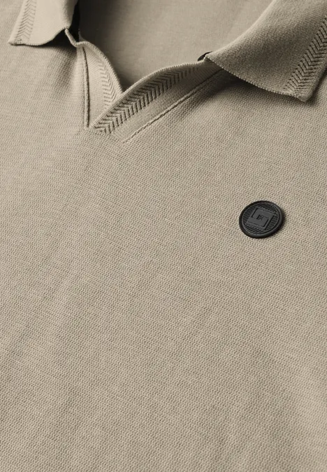 Gros plan sur un polo beige avec col et écusson rond noir, mettant en valeur la texture du tissu.