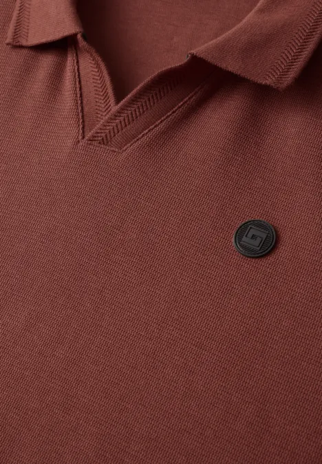Polo marron à col V avec petit badge rond logo sur la poitrine.
