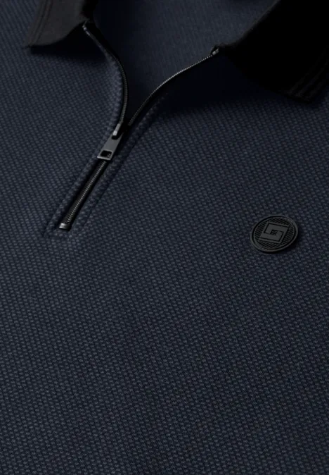Gros plan sur un polo bleu marine texturé, demi-zip et logo rond brodé sur la poitrine.