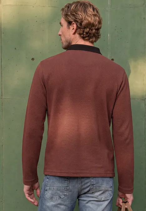 Homme vu de dos portant un pull marron et un jean devant un fond vert.