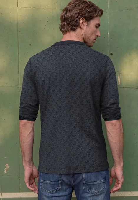 Langarm Poloshirt in Grafikprint dark ink blue Ein Mann steht vor einer grünen Wand, Rücken zum Betrachter, in einem dunkel gemusterten Poloshirt und Jeans.