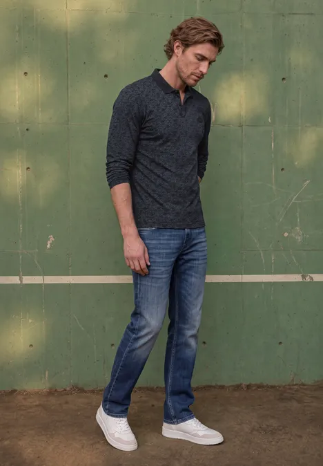 Langarm Poloshirt in Grafikprint dark ink blue Ein Mann in dunkelgrauem Shirt, Jeans und weißen Sneakern steht vor einer grünen Wand und schaut nach unten.