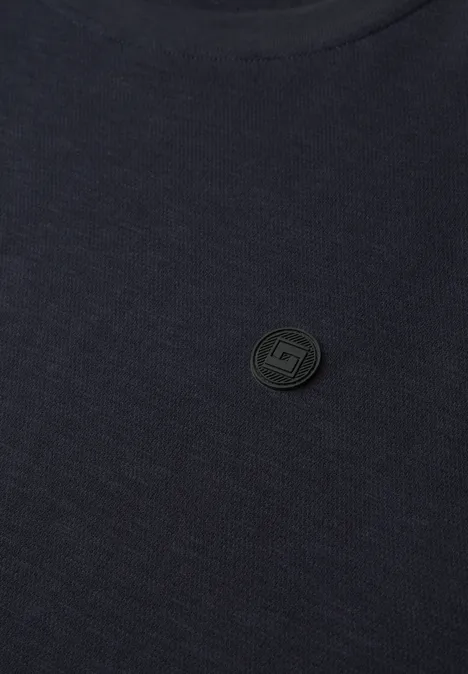 Nahaufnahme eines dunklen T-Shirts mit einem runden, dezenten Markenemblem.