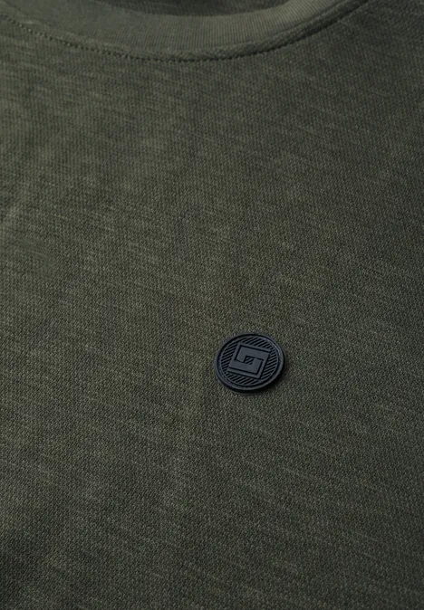 T-shirt vert en maille avec un badge circulaire noir sur la poitrine.