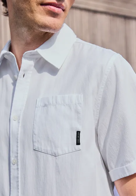 Ein Mann trägt ein weißes kurzärmeliges Hemd mit Brusttasche und schwarzem Etikett.