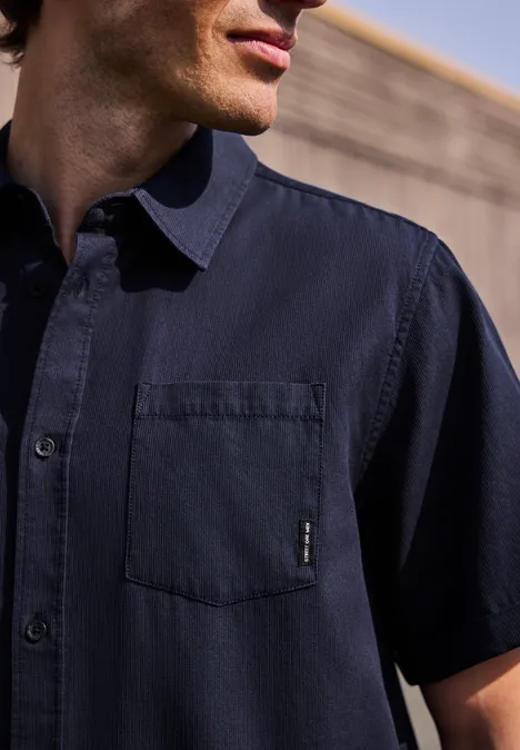 Nahaufnahme eines Mannes in einem kurzärmligen, dunkelblauen Hemd mit Brusttasche.