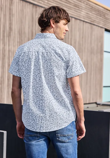 Ein Mann steht mit dem Rücken zur Kamera, trägt ein blau gemustertes Kurzarmhemd und Jeans.