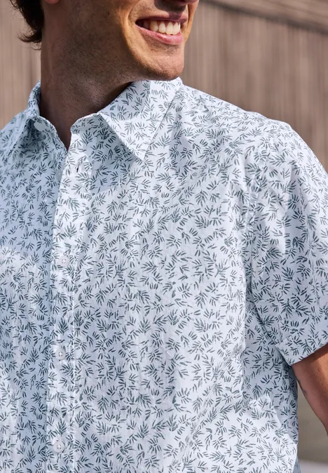 Mann in weißem Hemd mit blau-grünem Blattmuster lächelt.