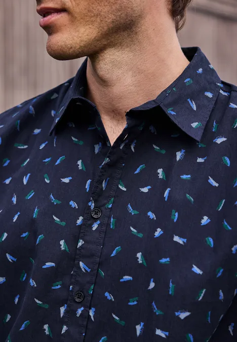 Ein Mann trägt ein navyblaues Hemd mit kleinem Fischmuster in Blau- und Grüntönen.