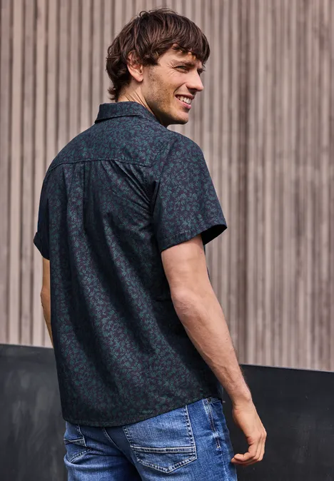 Mann von hinten in gemustertem Hemd und Jeans, schaut über die Schulter vor Holzverkleidung.