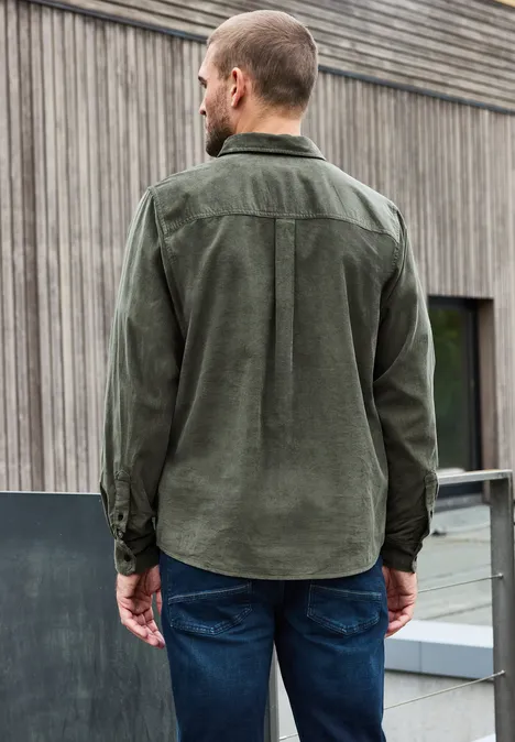 Mann von hinten in grüner Cordhemd und Jeans vor Holzfassade.