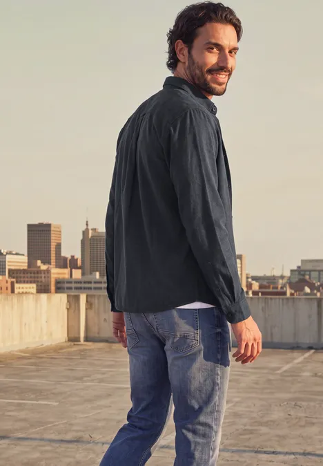 Ein Mann in Jeans und Jacke steht auf einem Dach und blickt über die Stadt.