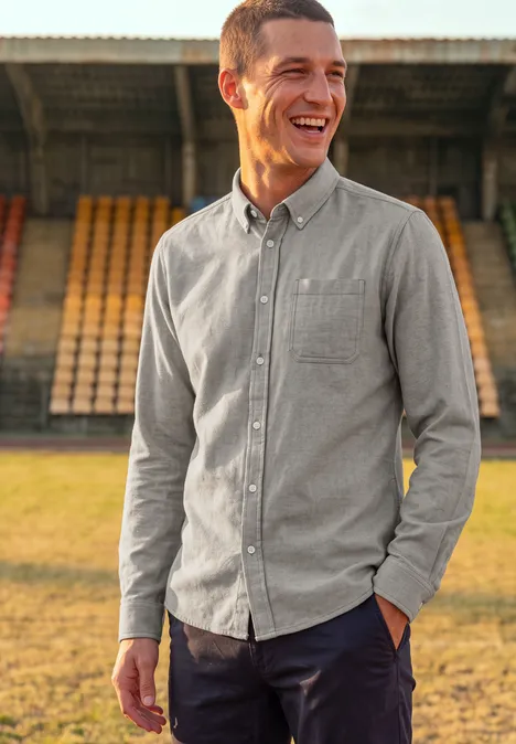 Ein freundlicher Mann in grauem Hemd lächelt vor leeren Tribünen im Stadion.
