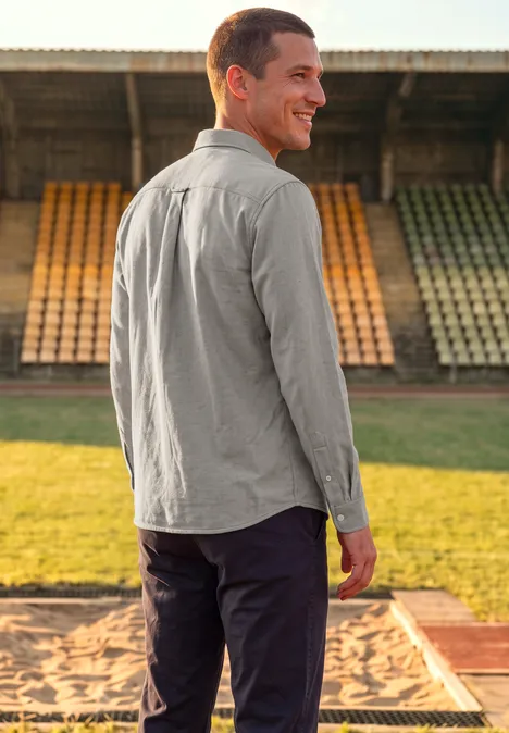 Ein Mann im grauen Hemd steht lächelnd im Stadion, Rücken zur Kamera, Blick über die Schulter.