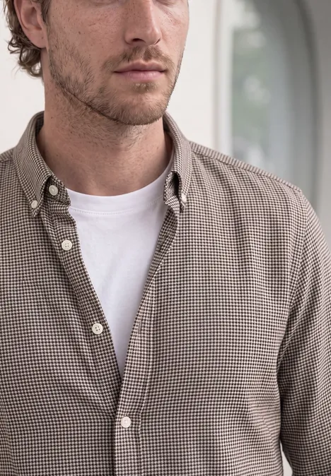 Portrait d’un homme portant une chemise à carreaux beige et un t-shirt blanc, regard de côté.