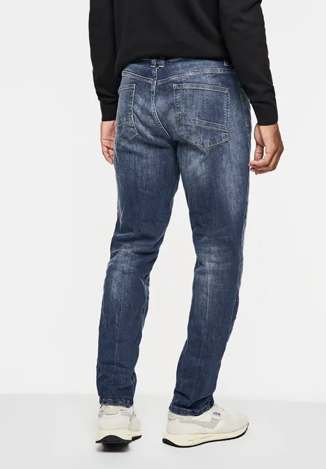 Jean used coupe droite indigo blue wash Mann in blauer Jeans und weißen Sneakern, Rückansicht, schwarzer Pullover.