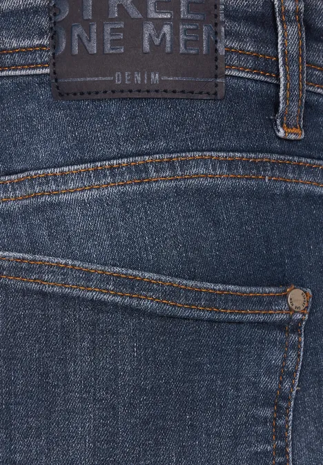 Jean used coupe droite indigo blue wash Nahaufnahme einer blauen Jeans mit Label und orangefarbenen Nähten.