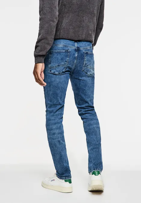 Person in blauer Jeans und weißen Sneakers von hinten.