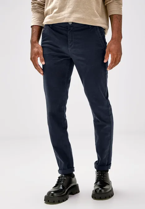 Mann trägt dunkelblaue Hose, beiges Oberteil und schwarze Schuhe.
