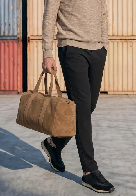 Iemand draagt een zwarte broek en houdt een bruine reistas vast voor gekleurde containers.