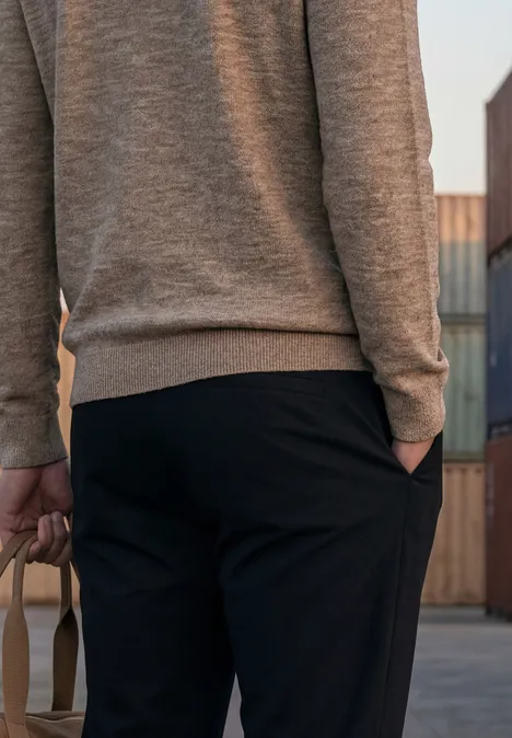 Vue de dos d'une personne en pull gris et pantalon noir tenant un sac, devant des conteneurs.