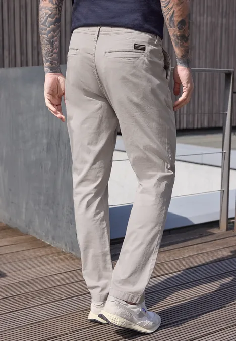 Ein Mann steht von hinten in hellen Chinohosen auf einer Holzterrasse neben einem Geländer.