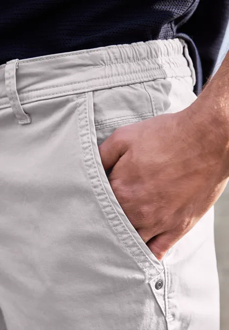 Eine Hand steckt in der Tasche einer hellbeigen Hose, seitlich am Körper.