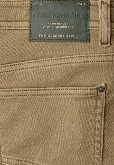 Beige herensbroek met zichtbare zak, label "The Classic Style" en contrasterende stiksels.