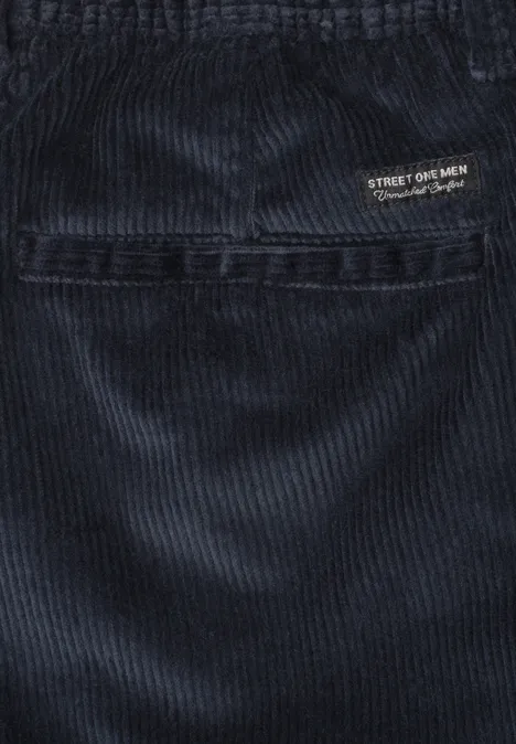 Close-up van donkerblauwe corduroybroek met zichtbare naad en klein logo-label.
