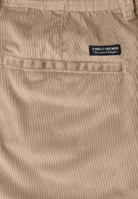Nahaufnahme eines beigen Cordstoffs mit Tasche und kleinem schwarzen Etikett am Bund.