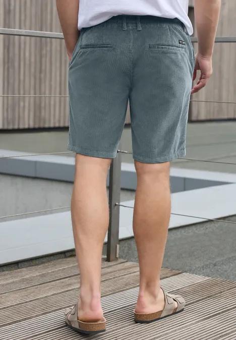 Rugzicht van een man in grijze short en sandalen op een houten terras.