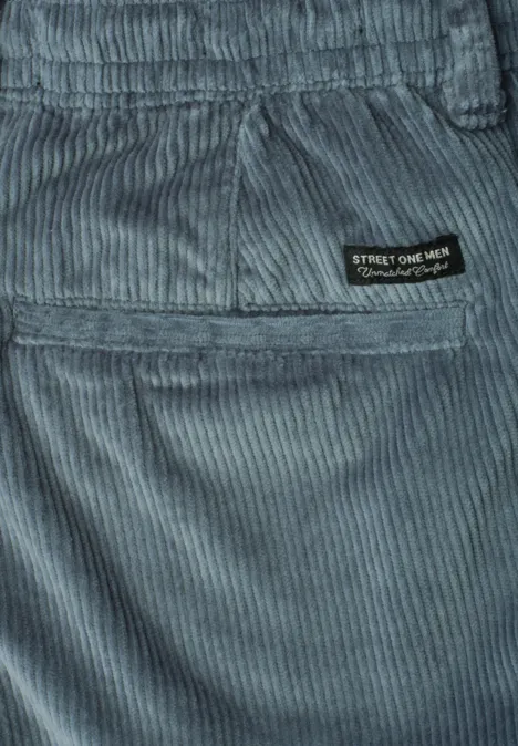 Close-up van een grijsblauwe corduroy broek met achterzak en zwart merklabel