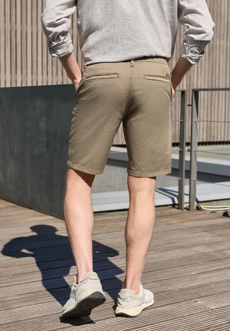 Ein Mann steht auf einer Holzterrasse, von hinten zu sehen in khakifarbenen Shorts und grauen Sneakern.