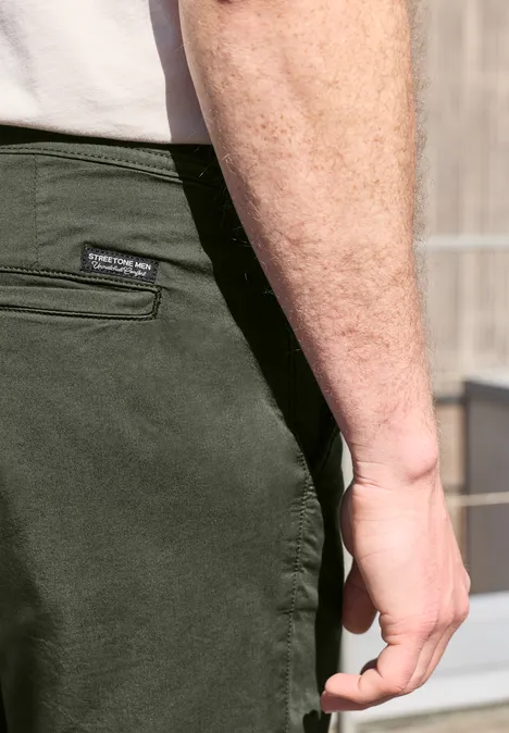 Close-up van een man in olijfgroene broek en wit T-shirt, met de hand naast de heup.