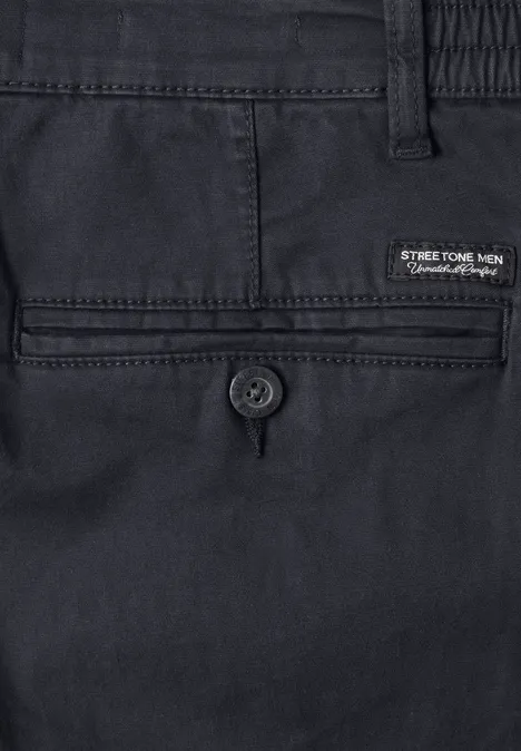 Close-up van een donkerblauwe herenbroek, achterzak met knoopsluiting en merklabel.
