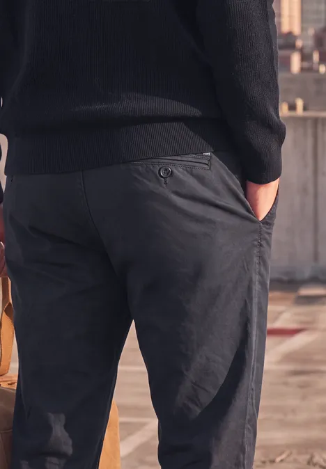 Close-up van een man van achteren in donkergrijze broek met handen in de zakken op een dak