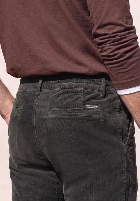 Ein Mann mit dunkelgrünen Cordhose und braunem Langarmshirt, Rückenansicht.