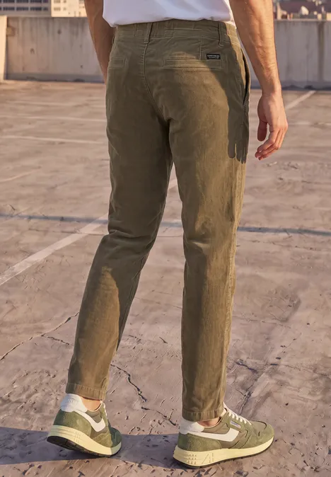 Ein Mann steht auf einem Betonparkdeck und trägt olivgrüne Hosen und weiße Sneaker.