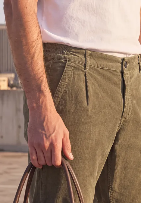 Nahaufnahme einer Person in weißem T-Shirt und olivgrüner Hose, die eine Tasche in der Hand hält.