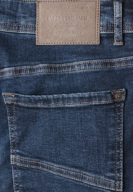 Close-up van een blauwe spijkerbroek met achterzak en lederen label boven de taille.