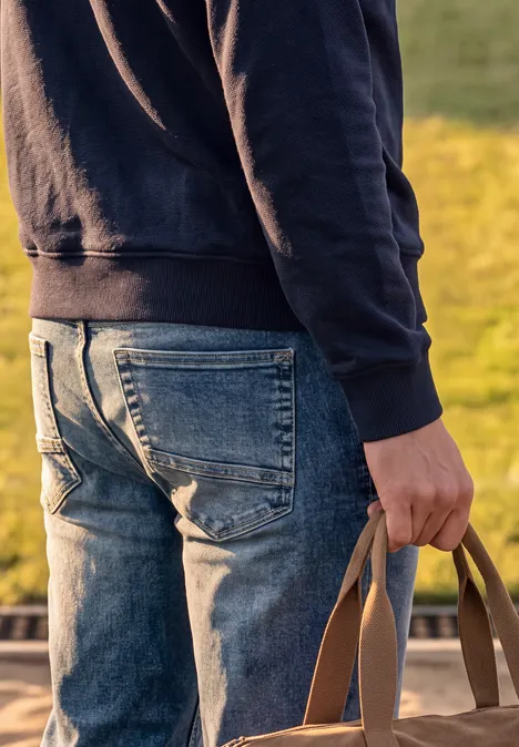 Slim Leg-jeans met Regular Fit soft greencast random wash Een persoon in spijkerbroek en hoodie van achteren gezien, met een tas in de hand.