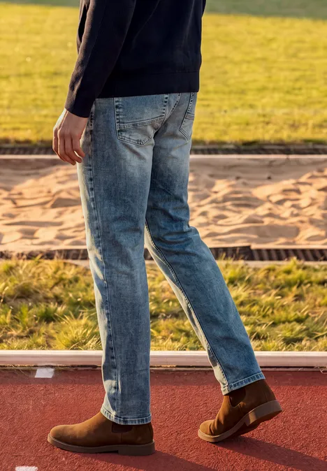 Straight Leg Jeans im Regular Fit soft greencast random wash Eine Person in Jeans und braunen Schuhen geht auf einer Sportbahn neben einer Sandgrube.