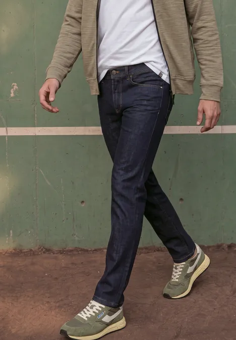 Ein Mann geht vorbei, trägt dunkle Jeans und grüne Sneaker vor einer grünen Wand.