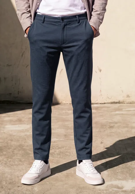 Eine Person trägt dunkelblaue Hose und weiße Sneaker vor einer hellen Wand.